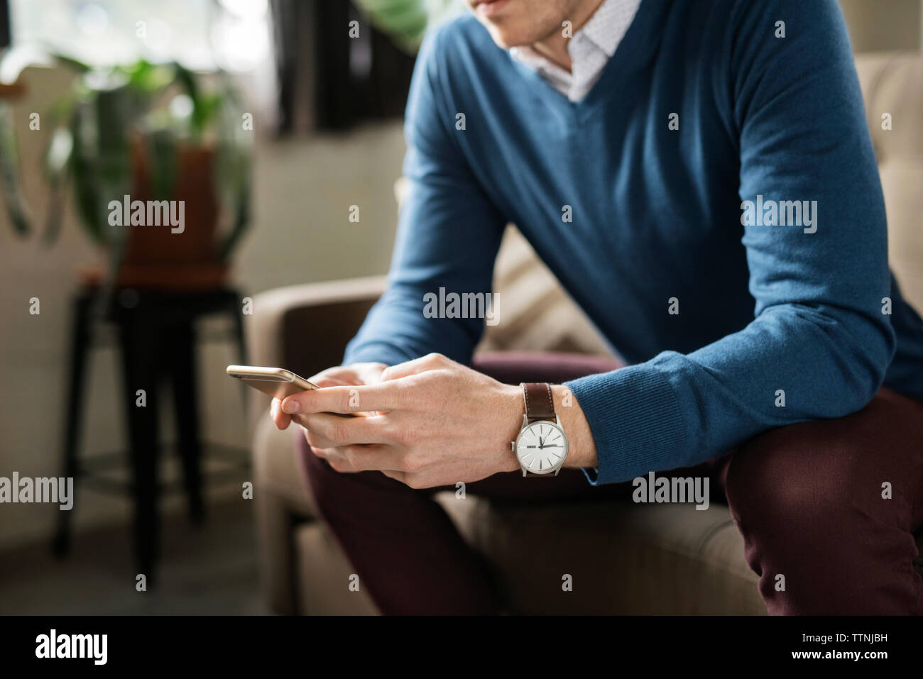 Sezione mediana dell'uomo utilizzando smart phone mentre è seduto sul divano Foto Stock