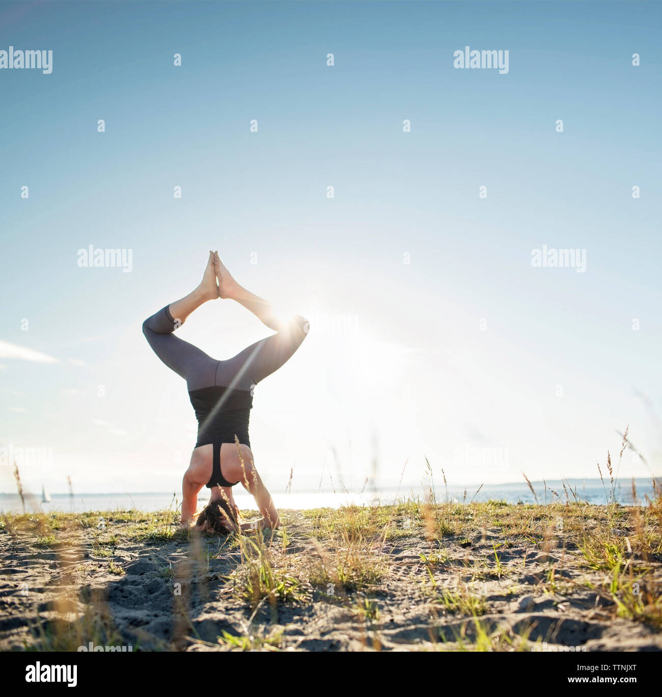 Vista posteriore della donna pratica angolo legato headstand pongono sulla sabbia di mare Foto Stock