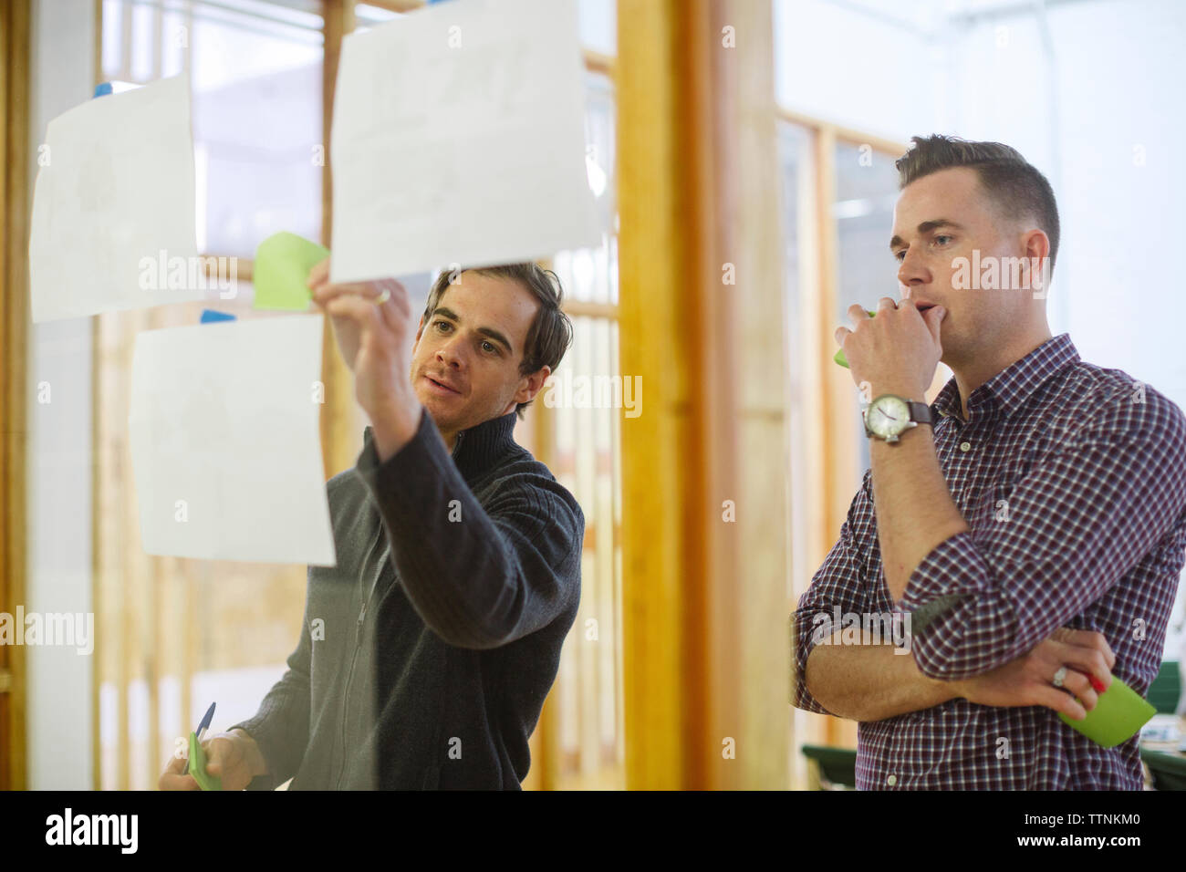 Colleghi di sesso maschile note di incollaggio su vetro in office Foto Stock