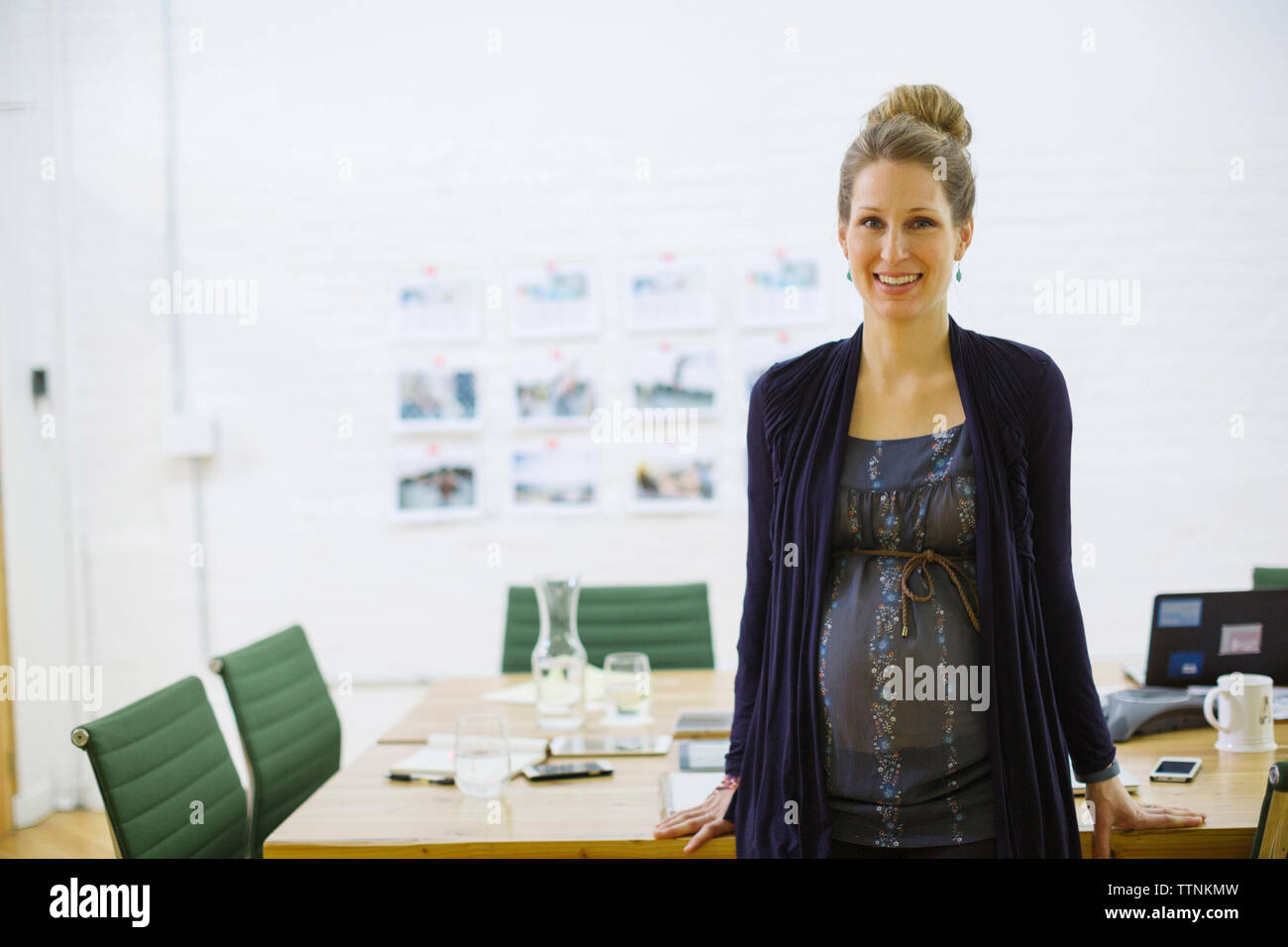 Ritratto di sorridente imprenditrice incinta in piedi da tavola nella sala riunioni Foto Stock