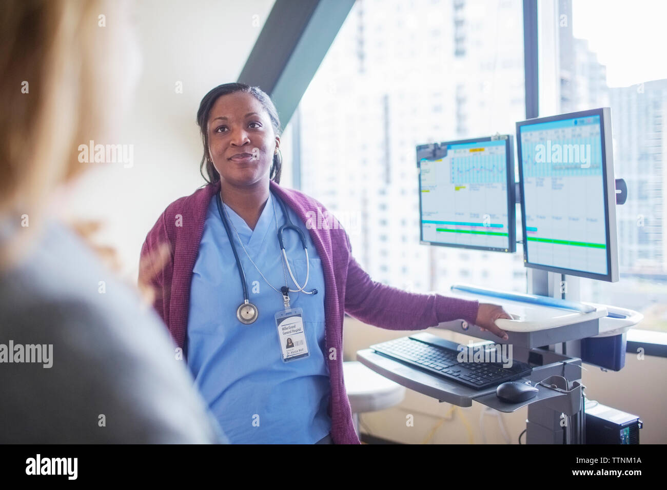 Medico donna guardando il paziente mentre in piedi dal computer desktop in sala medica Foto Stock