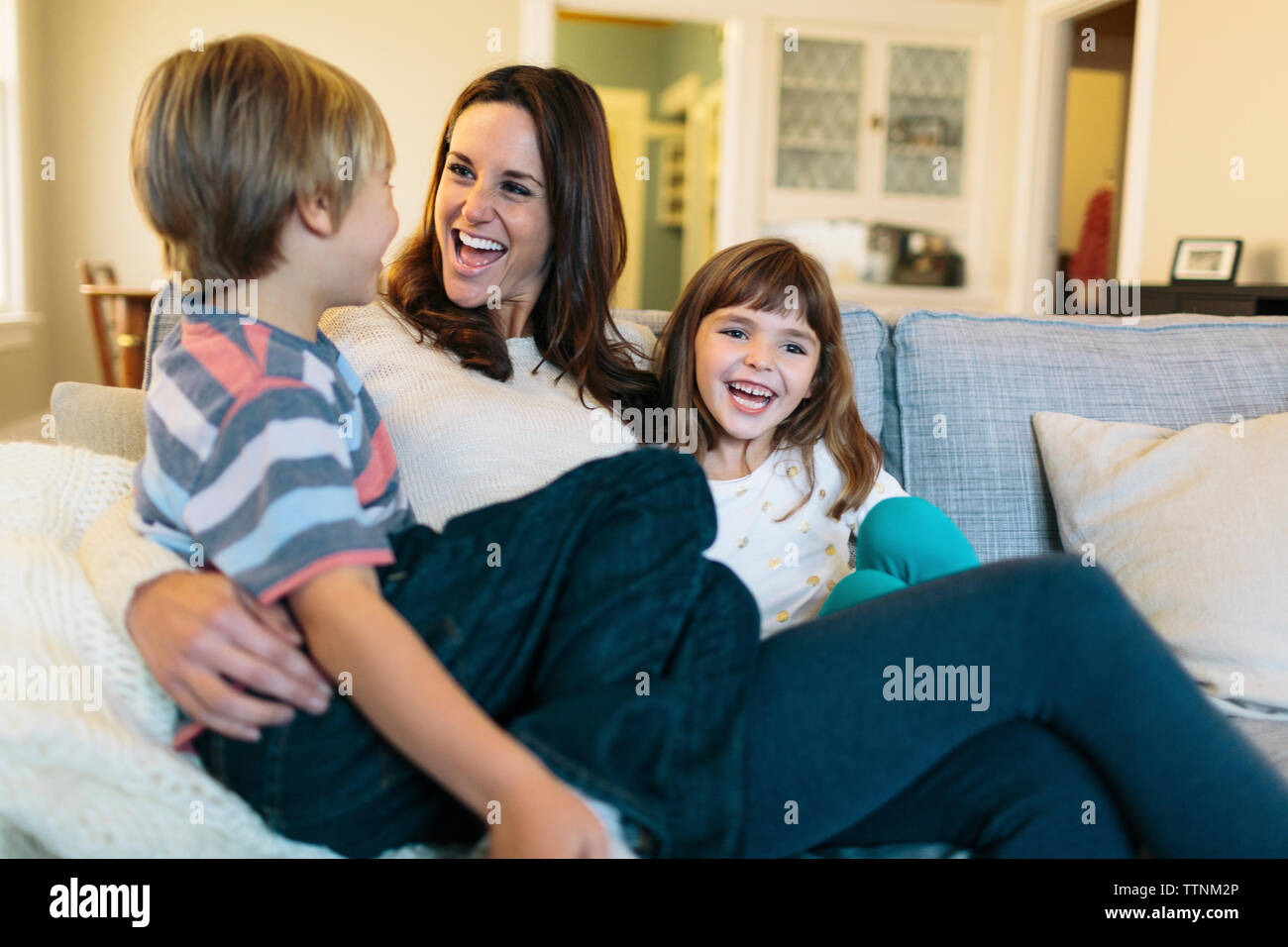 Allegro madre con bambini seduti sul divano di casa Foto Stock