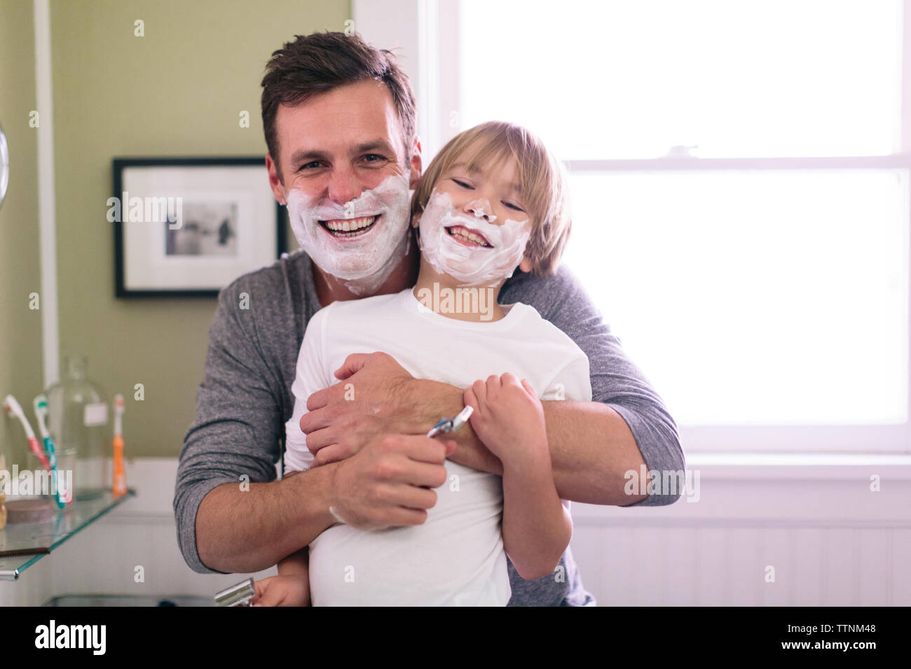 Ritratto di felice padre e figlio con crema di rasatura sulla faccia in piedi in bagno Foto Stock