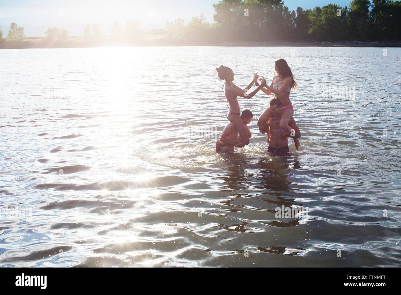 Amici di sesso maschile che trasportano donne sulle spalle mentre godendo nel fiume Foto Stock