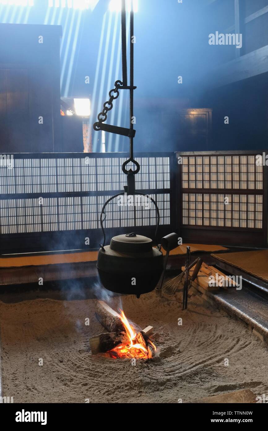 Tradizionale Giapponese o irori sunken tino mostra acceso il fuoco con ghisa nera bollitore sospesa al di sopra di esso, schermi dietro di essa e luce in streaming Foto Stock