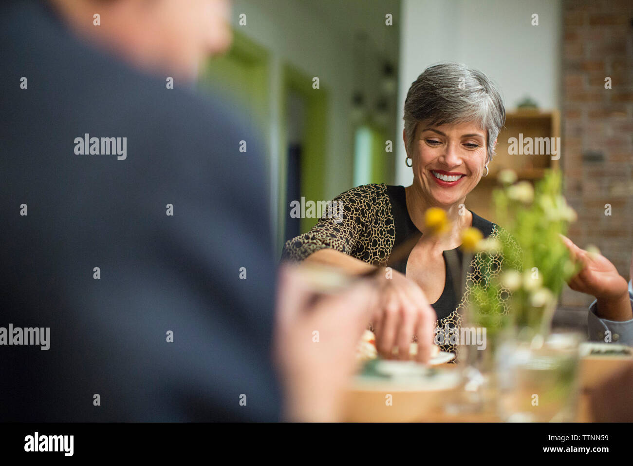 Donna sorridente al tavolo durante la riunione sociale Foto Stock