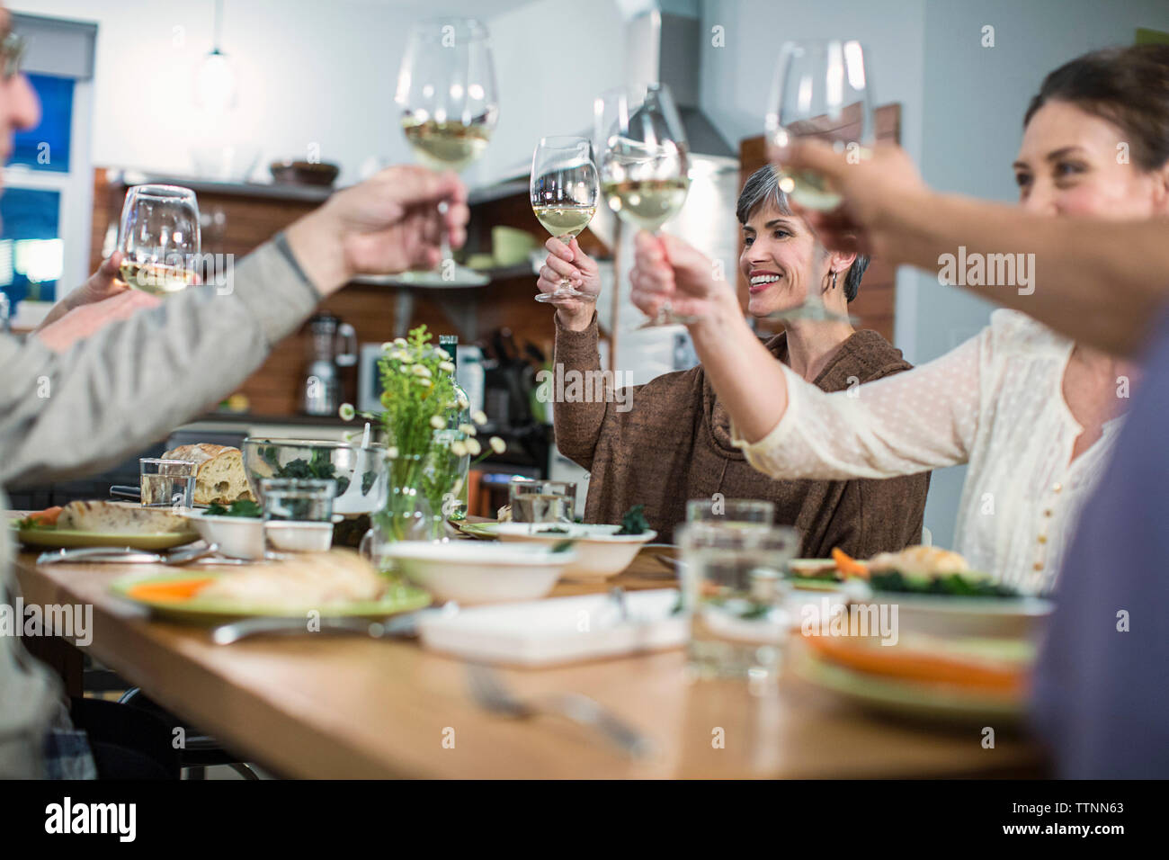 Happy amici vino di tostatura mentre è seduto al tavolo durante la riunione sociale Foto Stock