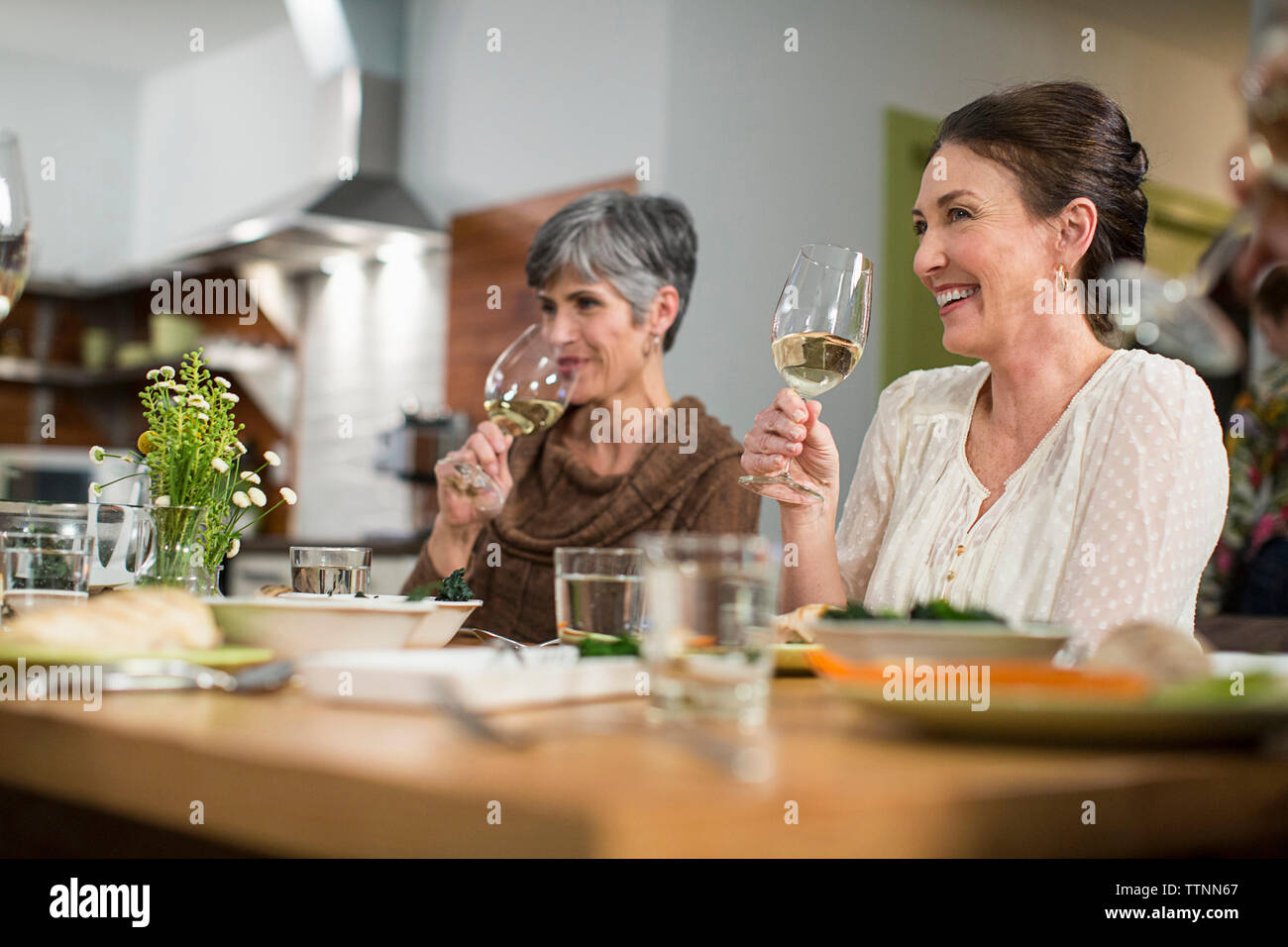 Donna sorridente amici bevendo vino seduti a tavola durante la riunione sociale Foto Stock