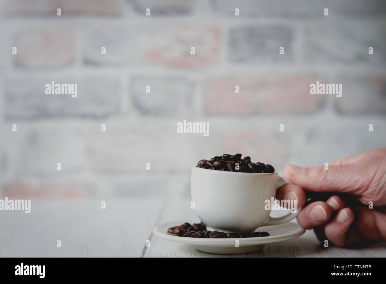 Ritagliato mano azienda cup con i chicchi di caffè contro un muro di mattoni sul tavolo di legno Foto Stock