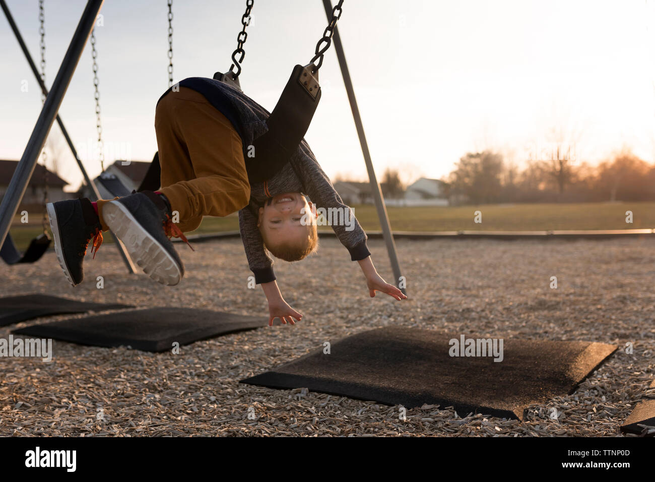 Ritratto di felice ragazzo appoggiato capovolto su swing sul parco giochi Foto Stock