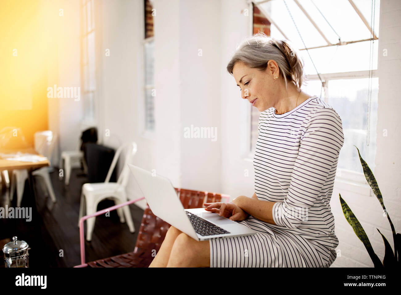 Donna matura utilizzando computer portatile mentre seduta nel salotto di casa Foto Stock