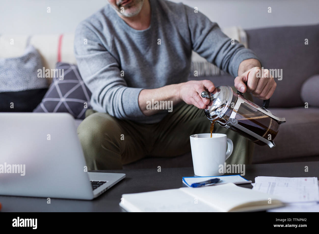Sezione mediana dell'uomo versando il caffè dalla stampa francese nella tazza in casa Foto Stock
