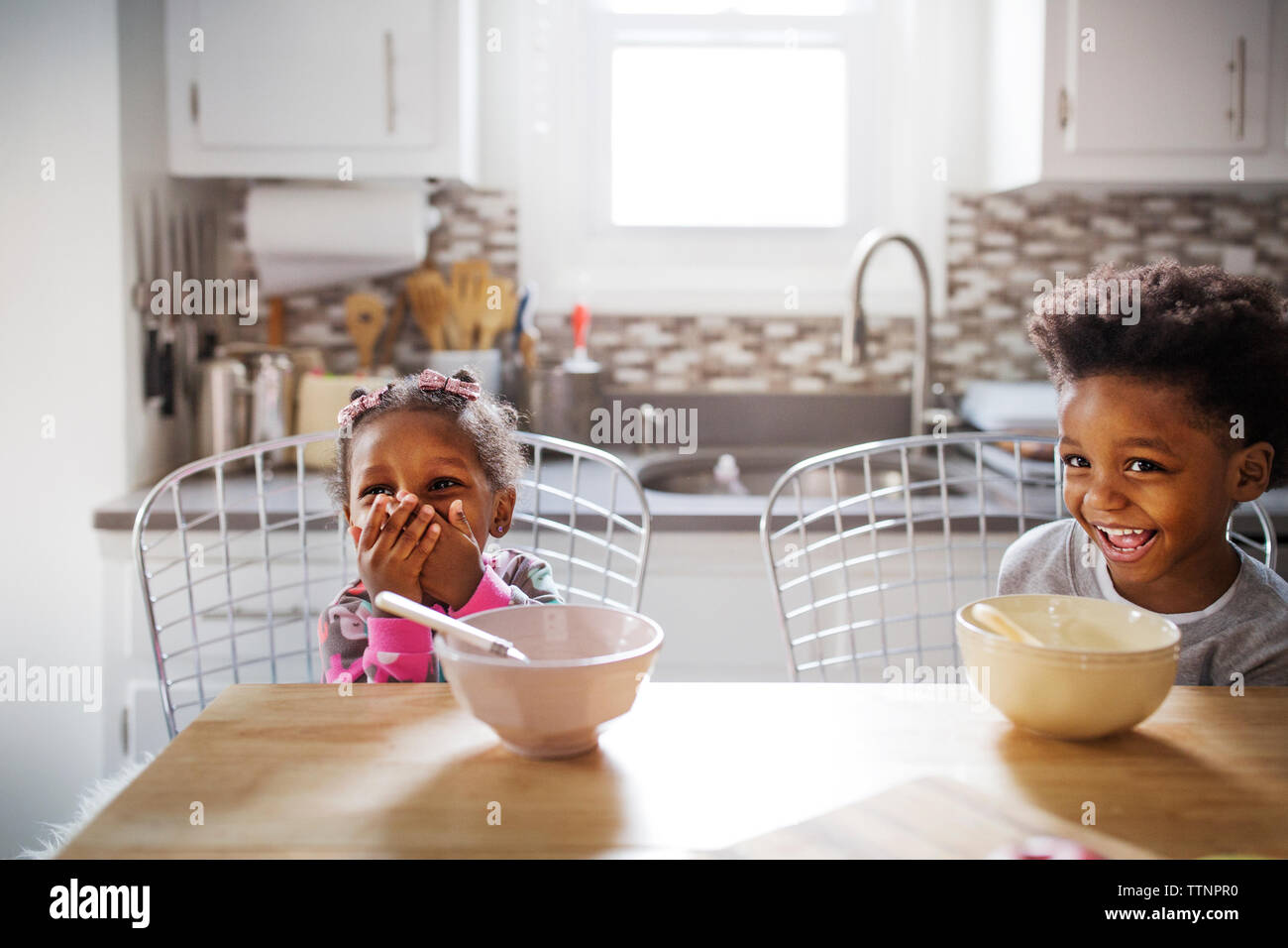 Allegro fratello e sorella che guarda lontano mentre si consuma la colazione nella cucina Foto Stock