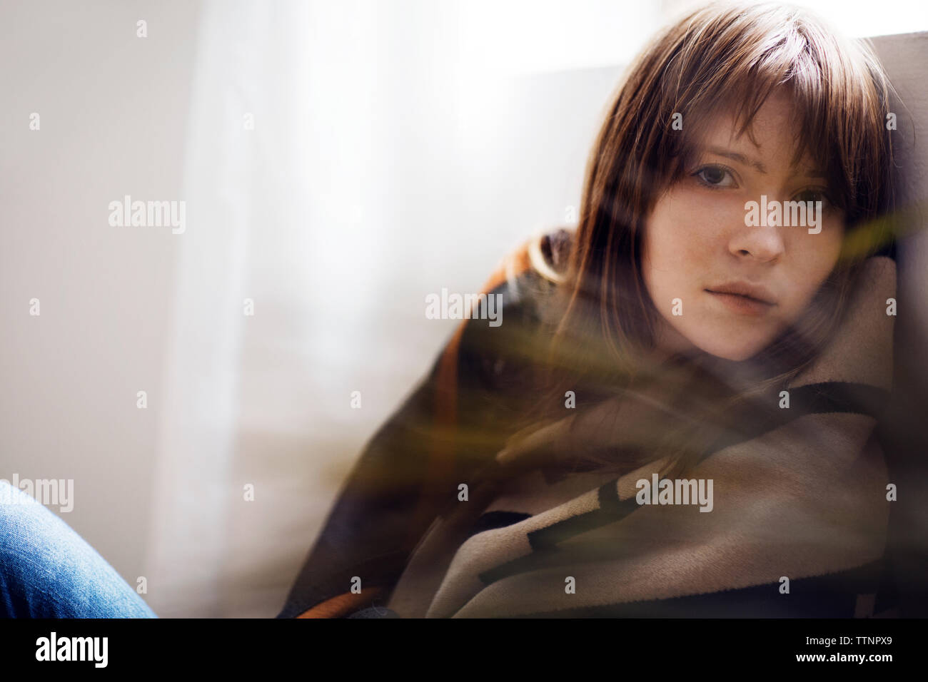 Ritratto di donna triste avvolto in seduta coperta dalla finestra a casa Foto Stock