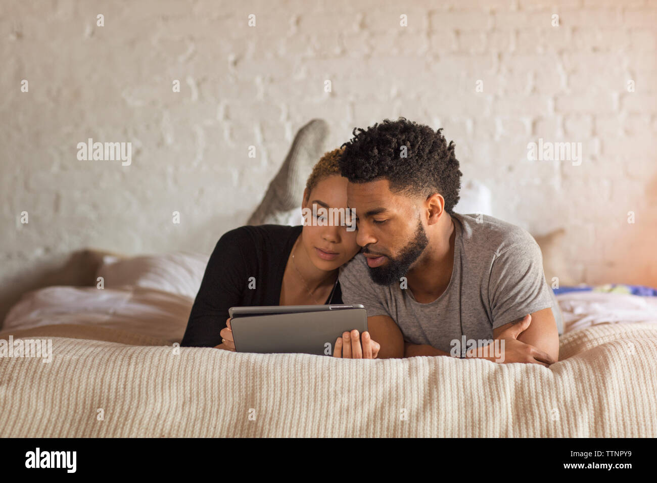 Multi-etnico giovane utilizzando computer tavoletta mentre giaceva sul letto di casa Foto Stock