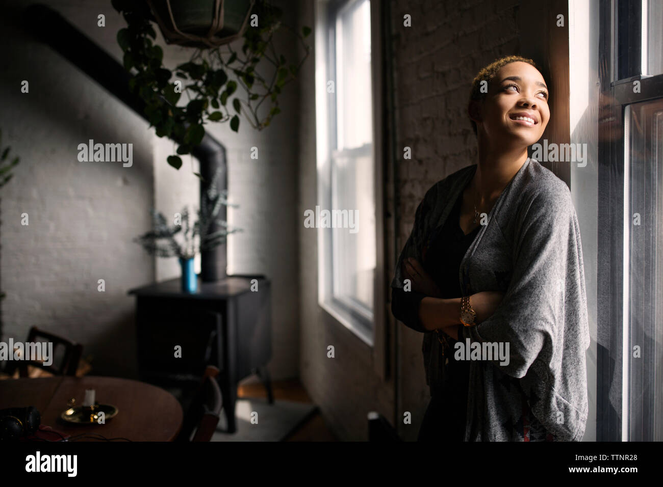 Felice donna in piedi con le braccia incrociate per finestra Foto Stock