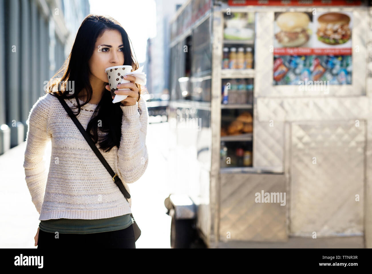 Giovane donna di bere il caffè dal bicchiere monouso con concessione di stand in background Foto Stock