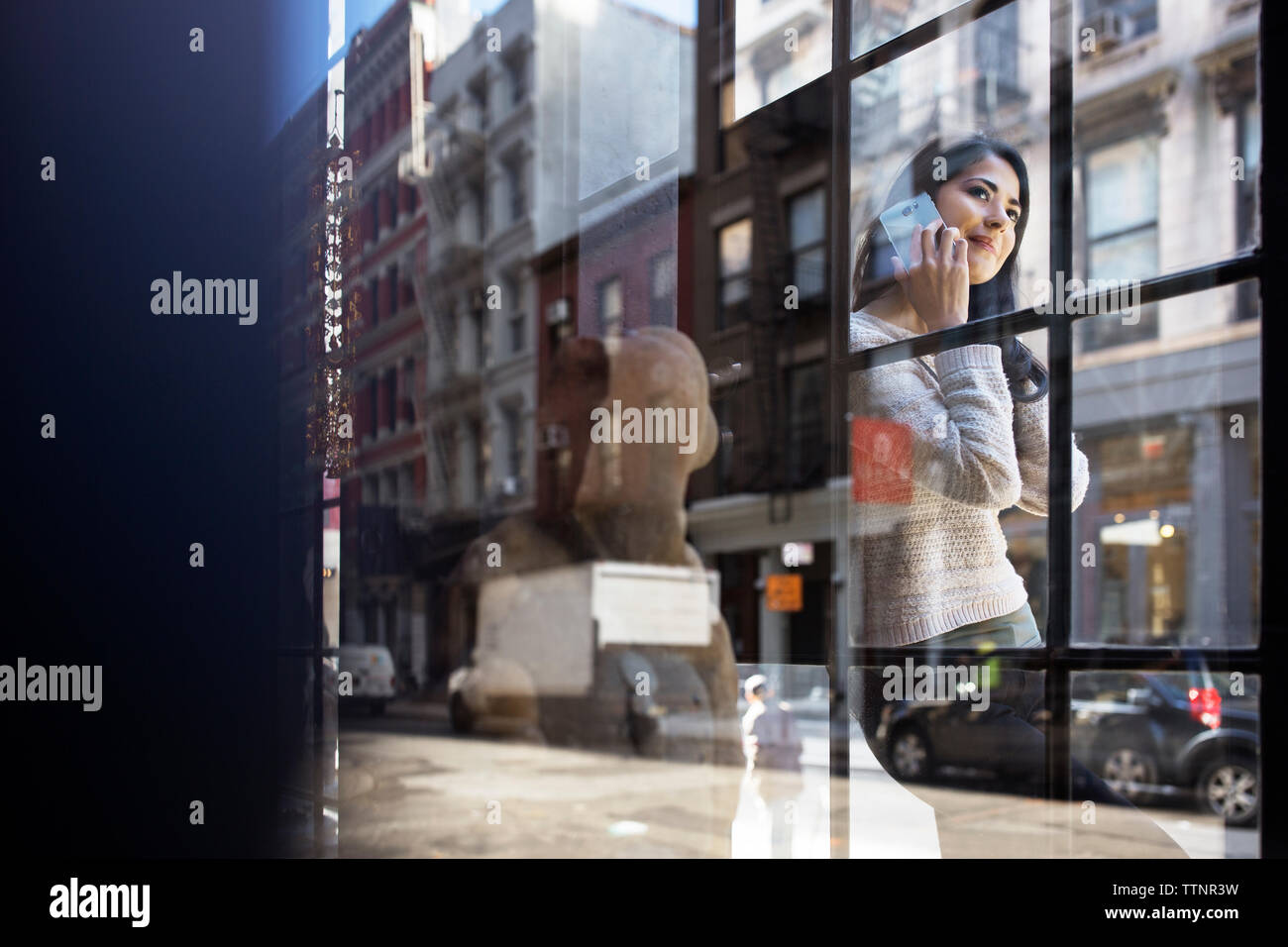 Giovane donna rispondendo alle smart phone visto attraverso la parete in vetro Foto Stock