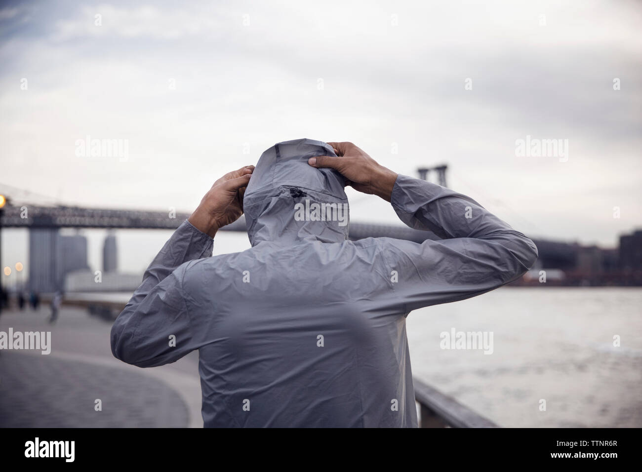 Vista posteriore di atleta maschio indossando giacca con cappuccio con Williamsburg Bridge in background Foto Stock