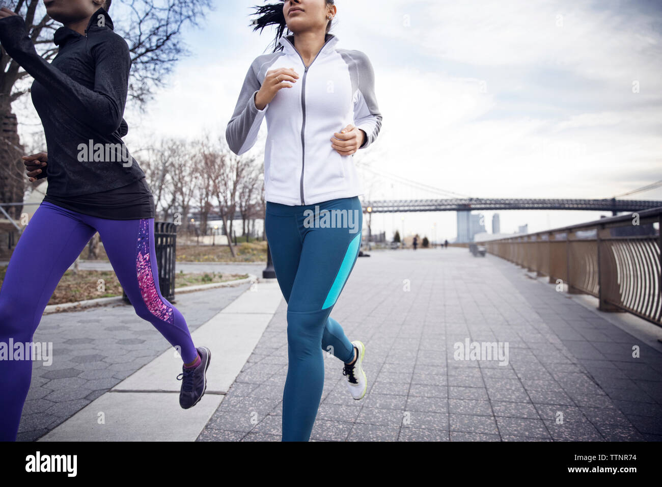 Sezione bassa delle atlete in esecuzione sul sentiero con Williamsburg Bridge in background Foto Stock