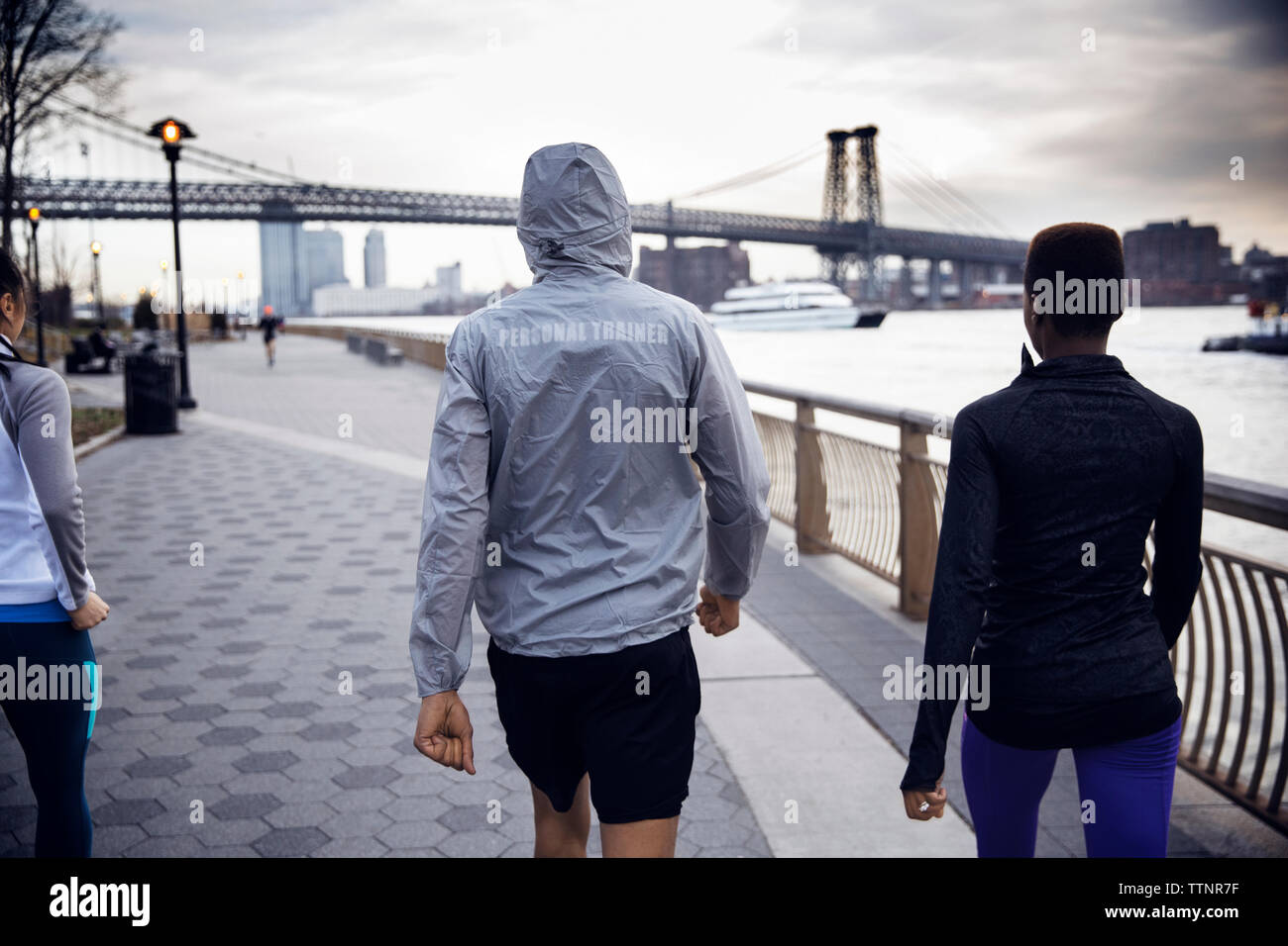 Vista posteriore di atleti camminando sul sentiero con Williamsburg Bridge in background Foto Stock