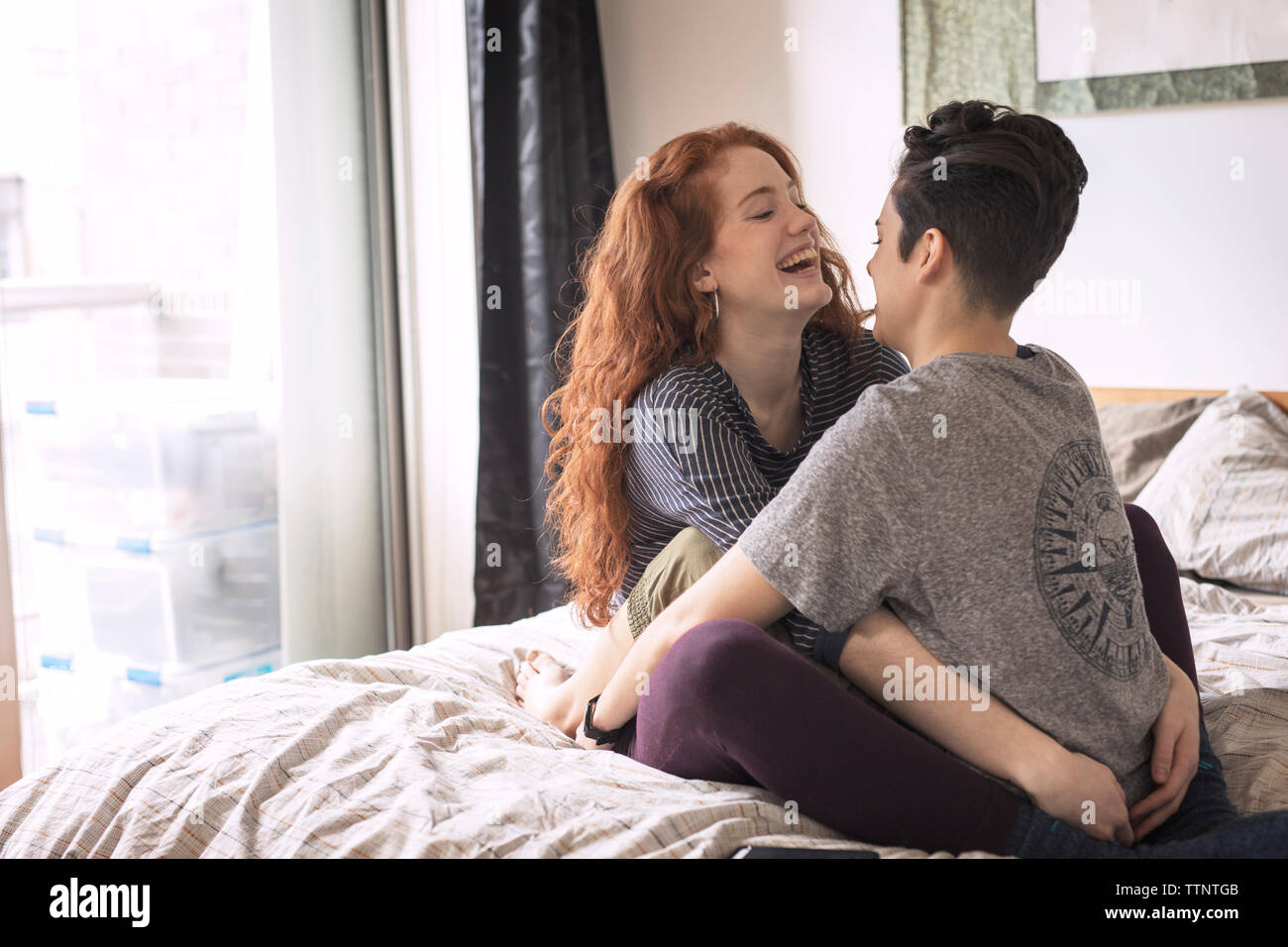 Allegro lesbiche seduta faccia a faccia sul letto di casa Foto Stock