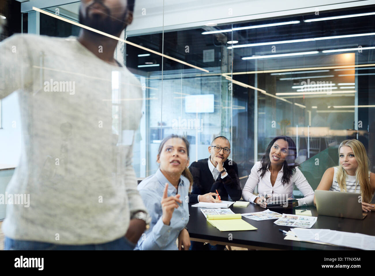 Multi-etnico colleghi guardando imprenditore dando la presentazione in riunione a board camera Foto Stock