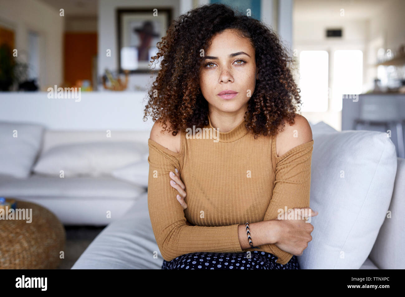 Ritratto di donna fiducioso con le braccia incrociate seduti sul divano di casa Foto Stock