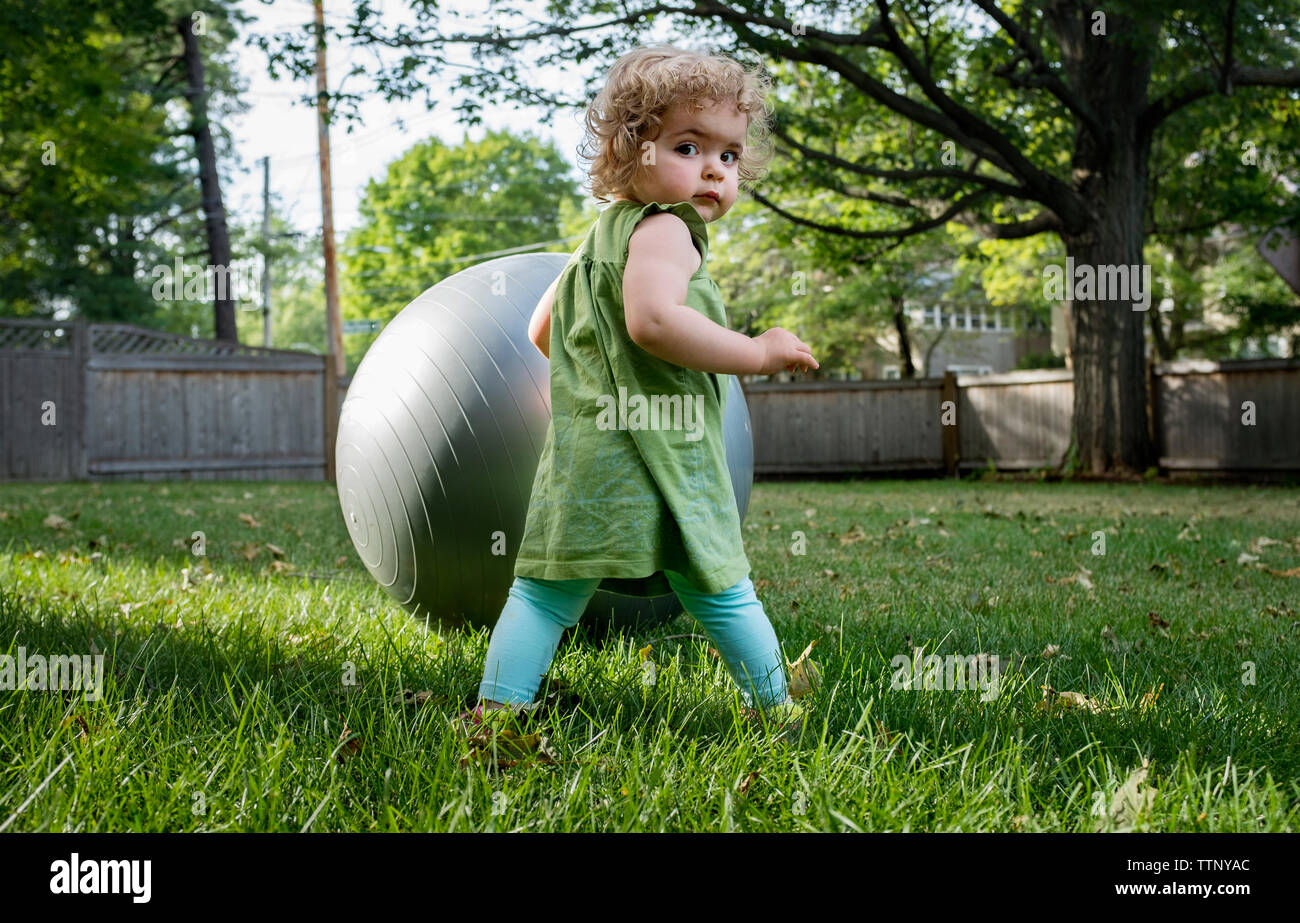 Vista posteriore del ritratto di Cute girl in piedi con la palla fitness a prato Foto Stock