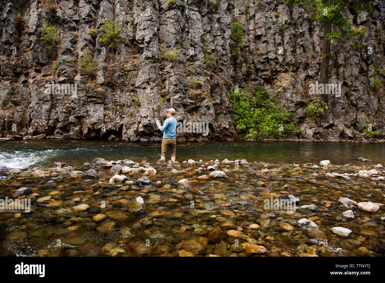 Vista posteriore dell'uomo di Pesca a Mosca Report di pesca in fiume contro formazioni di roccia Foto Stock