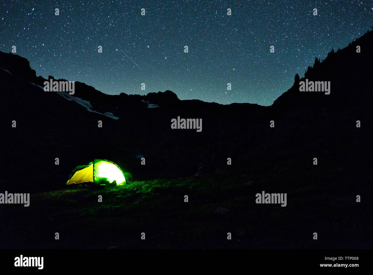 Tenda illuminata sulla montagna di silhouette di notte Foto Stock