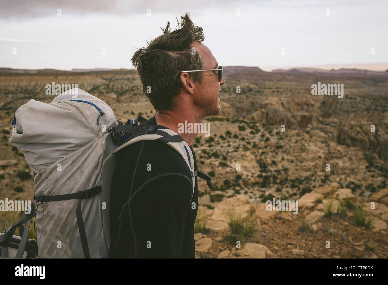 Vista laterale di un escursionista che guarda lontano mentre trasportano uno zaino contro semi-arido paesaggio Foto Stock