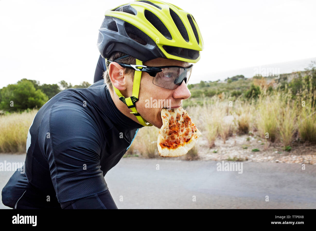 L'uomo mangiare la pizza mentre il ciclismo su strada contro il cielo chiaro Foto Stock