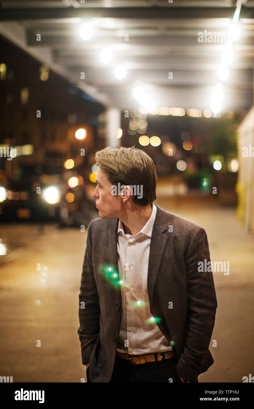 Uomo che indossa convenzionale in piedi sul marciapiede illuminato di notte Foto Stock