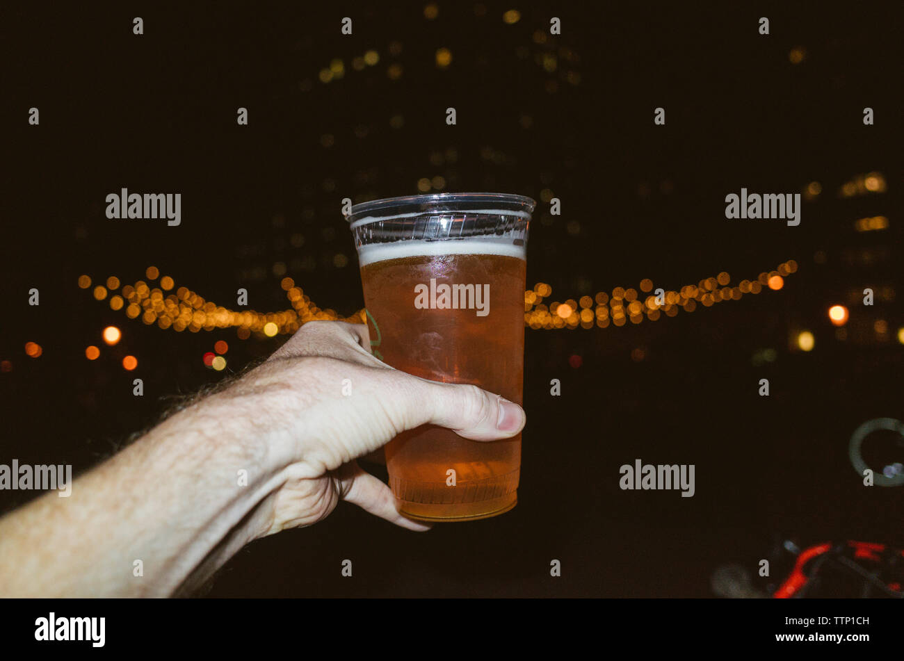 Ritagliate la mano di uomo con la birra contro luci illuminate di notte Foto Stock