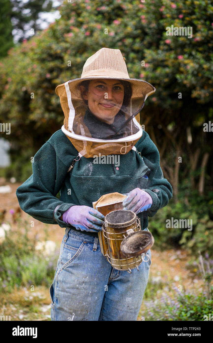 Ritratto di donna apicoltore indossando indumenti da lavoro protettiva permanente, mentre a livello di azienda Foto Stock