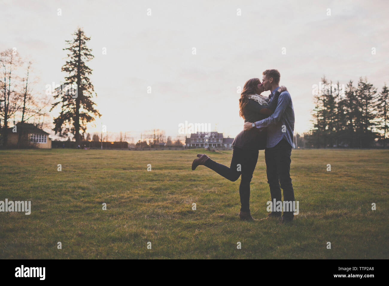 Coppia romantica baciare mentre si sta in piedi sul campo erboso contro sky Foto Stock