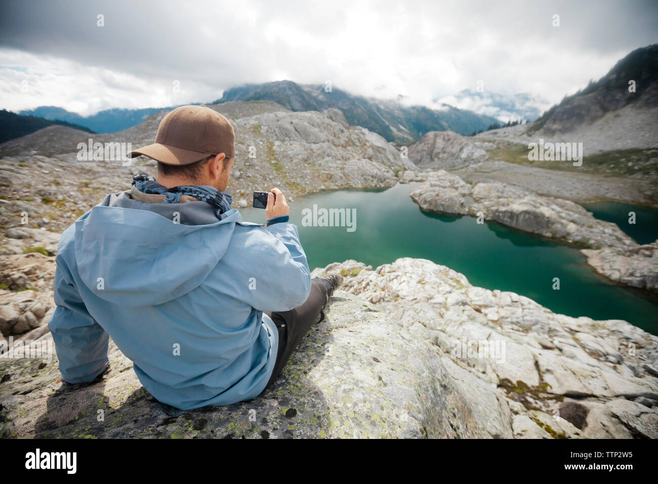 Vista posteriore di un escursionista fotografare mentre è seduto sulla scogliera a Garibaldi Provincial Park Foto Stock