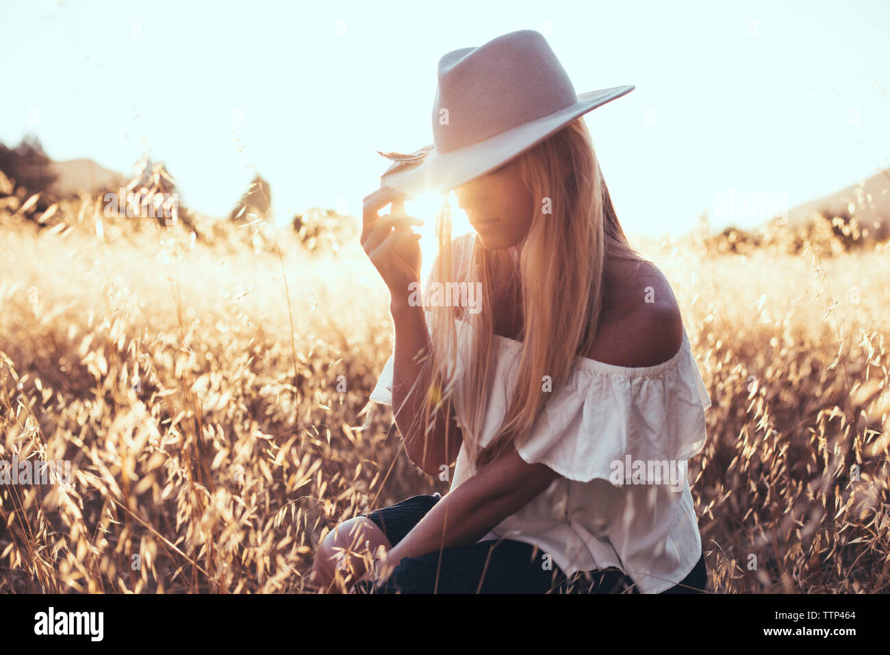 La donna nel cappello per il sole seduti sul campo nel mezzo di piante Foto Stock