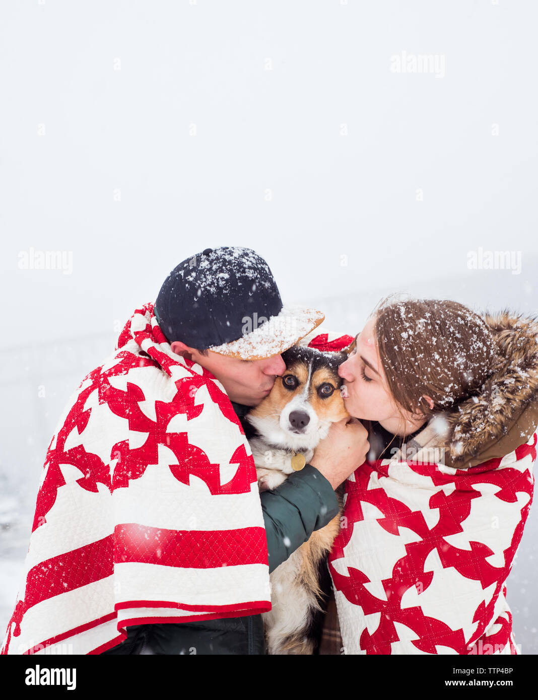 Giovane & cane huddle in coperta durante la nevicata & kiss dog insieme Foto Stock