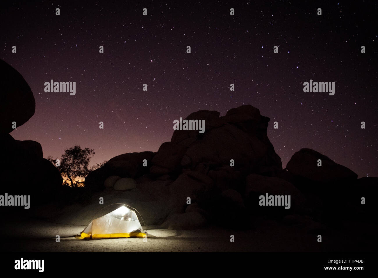 Tenda illuminata dalla formazione di roccia contro il cielo stellato Foto Stock