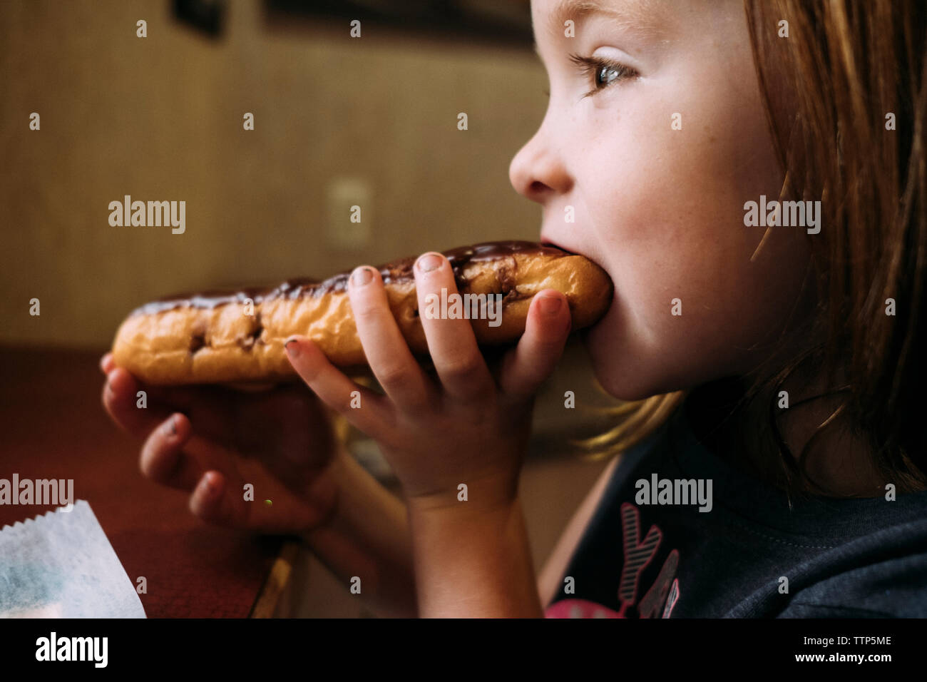 Vista laterale della ragazza carina di mangiare cibo dolce mentre è seduto a casa Foto Stock