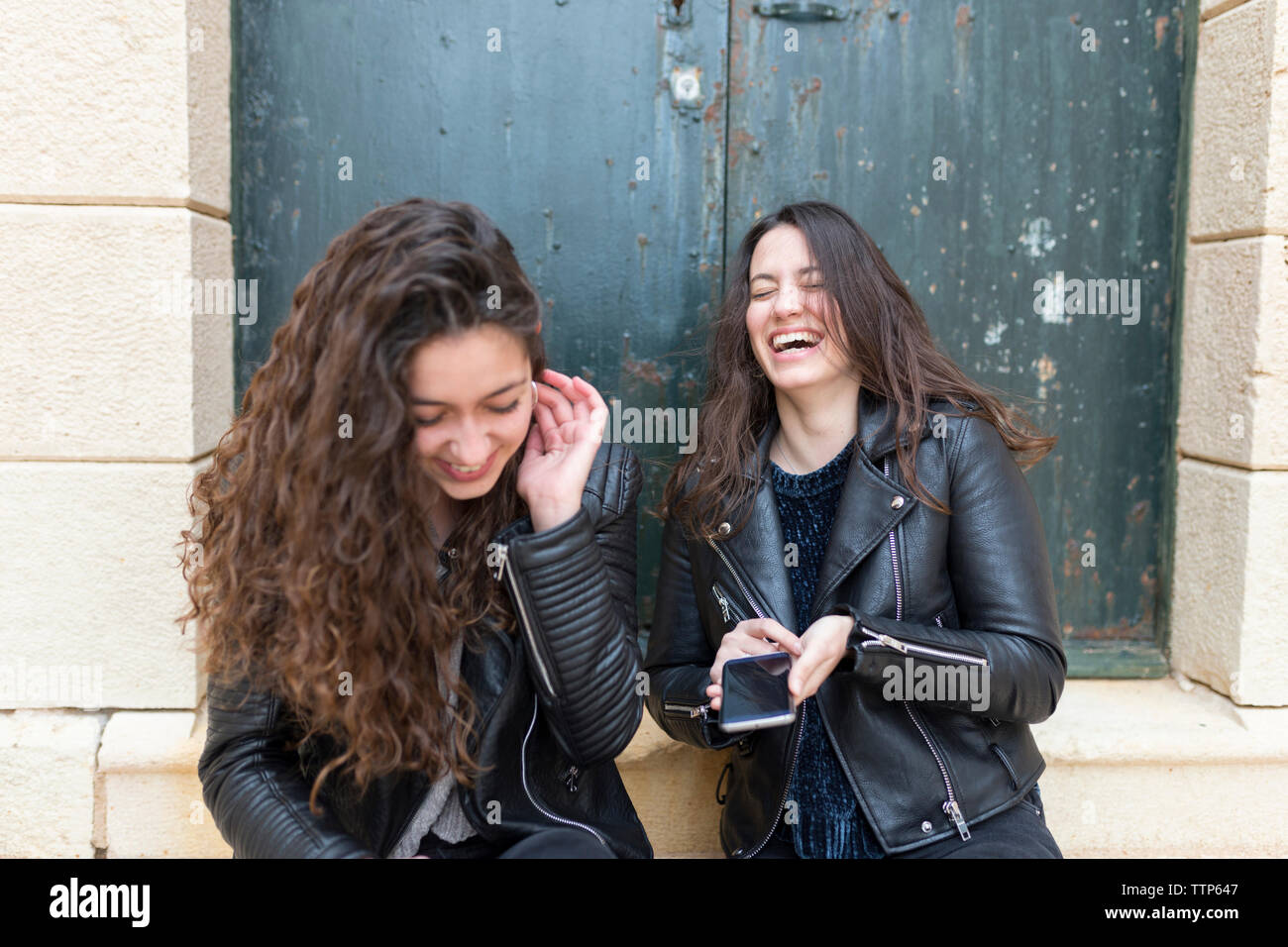 Happy amici utilizzando smart phone seduti dalla porta Foto Stock