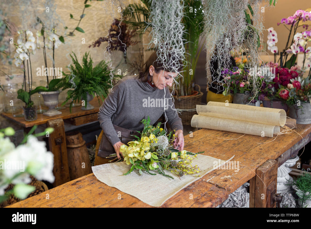 Senior donna disponendo bouquet di fiori al negozio di fiori scrivania Foto Stock