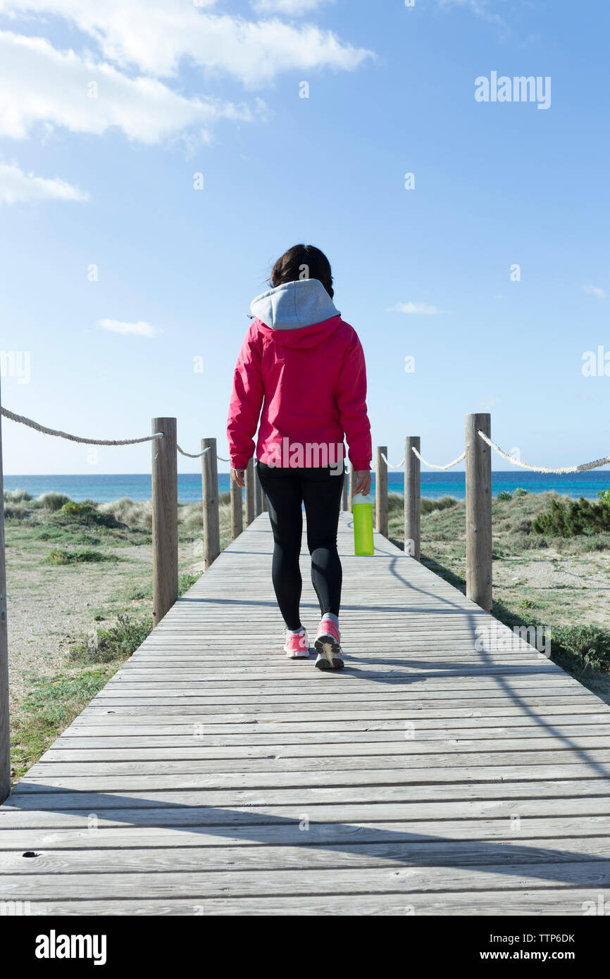 Vista posteriore della giovane donna di camminare sulla spiaggia di legno sentiero Foto Stock
