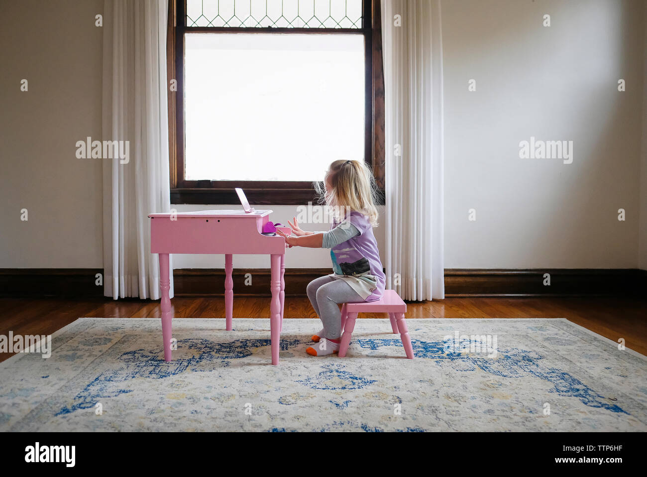 Vista laterale della ragazza che gioca toy piano contro la finestra a casa Foto Stock