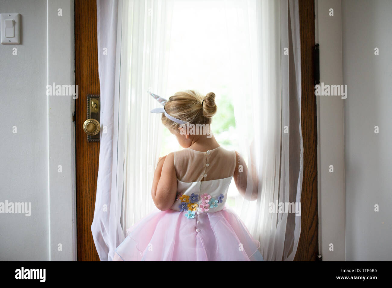 Vista posteriore della ragazza bionda con archetto unicorn nella porta guardando fuori Foto Stock
