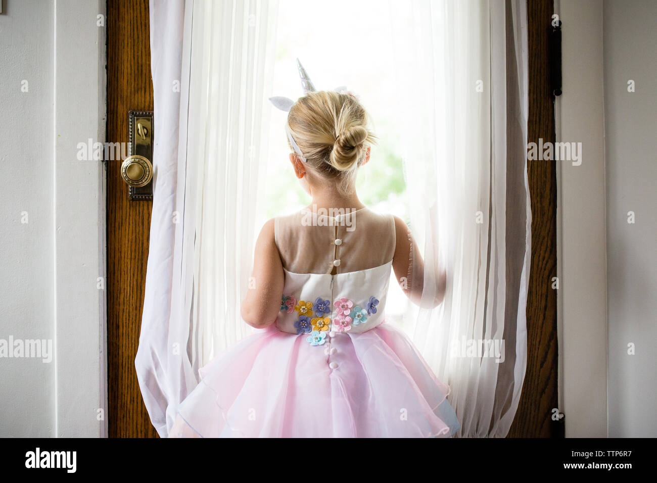 Piccola ragazza bionda con archetto unicorn guardando fuori della porta anteriore Foto Stock