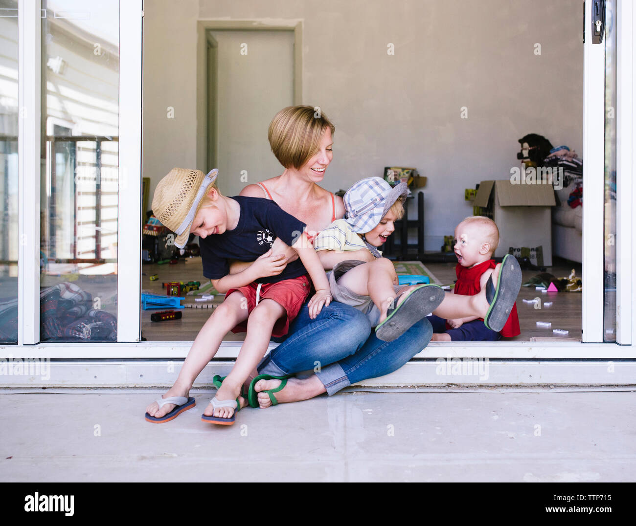 La madre a giocare con i bambini seduti sulla porta di casa Foto Stock