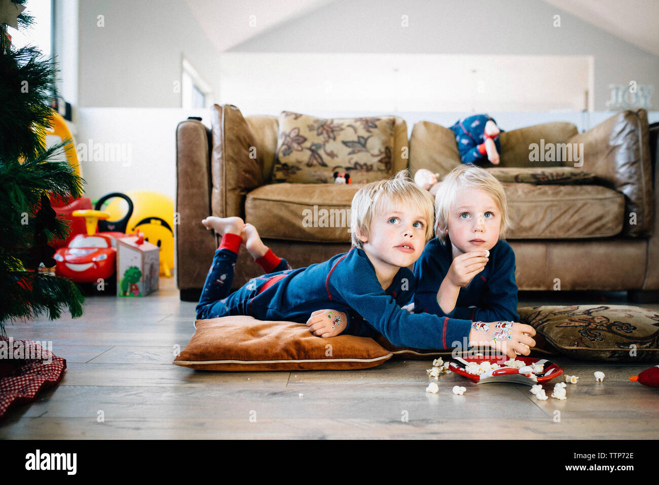 Fratelli che mangiano popcorn mentre guardano la TV a casa durante il natale Foto Stock